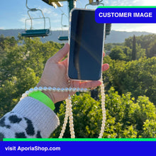 Load image into Gallery viewer, Image of customer holding Aporia Magsafe Clear Case - Pearl Crossbody Strap for iPhone 15/14/13/12 while riding chairlift zipline
