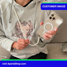 Load image into Gallery viewer, Image of customer holding the Aporia Magsafe Clear Case - Pearl Crossbody Strap for iPhone 15/14/13/12 while on a lobby
